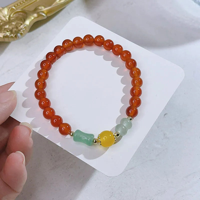 Close-up of a red agate bracelet with a dragon charm and Lucky Bag symbol on a wrist.