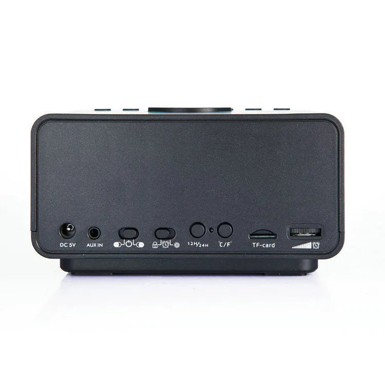 Black and white wireless alarm clock Bluetooth speaker with remote control on a table.