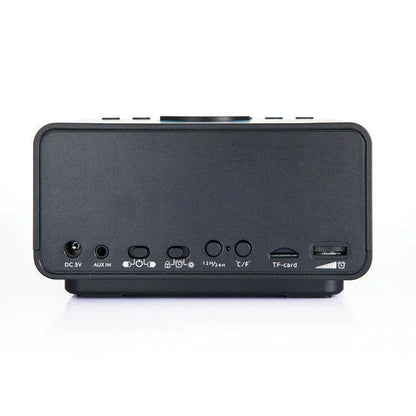 Black and white wireless alarm clock Bluetooth speaker with remote control on a table.