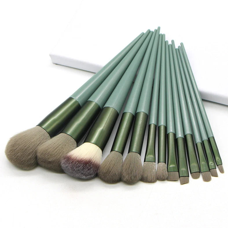 13 green makeup brushes with plastic handles and aluminium ferrules arranged with storage bag