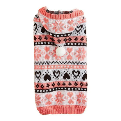 Small dog wearing a pink camouflage patterned knitted sweater with snowflake and heart stripes.
