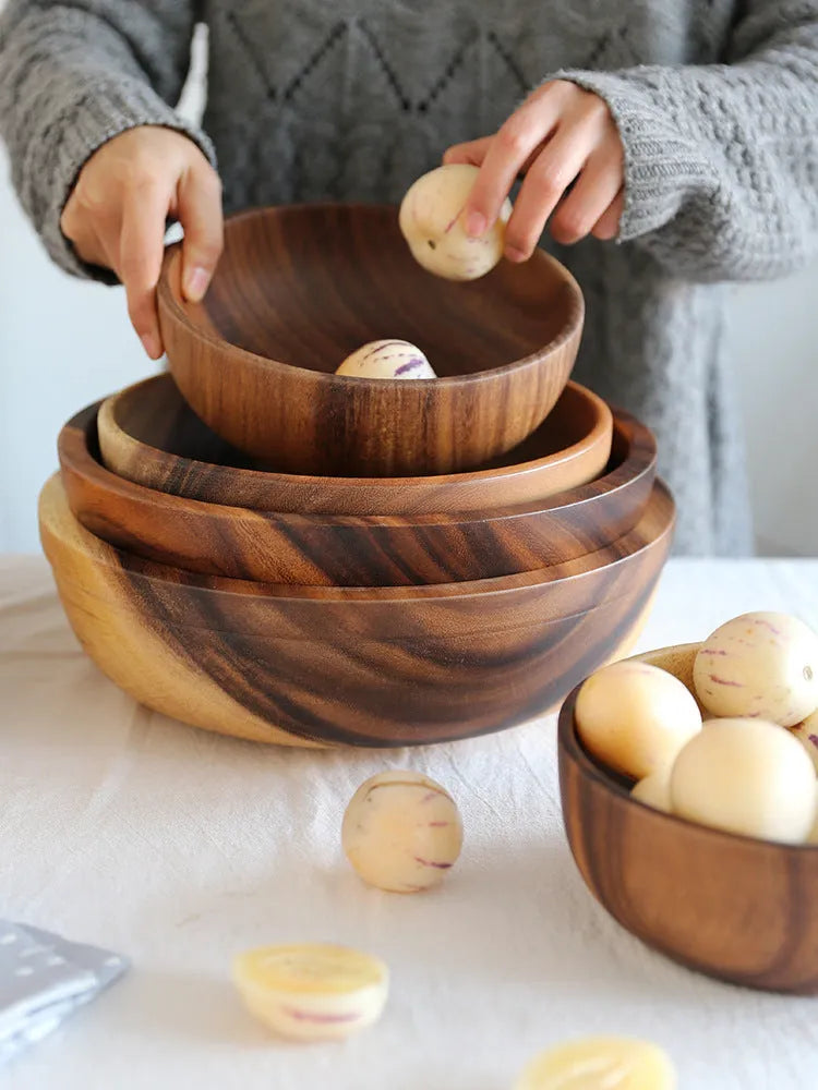 Set of five brown wooden bowls in different sizes on a wooden table, showing natural grain.
