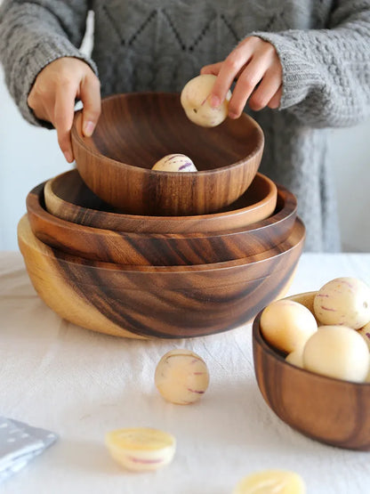 Set of five brown wooden bowls in different sizes on a wooden table, showing natural grain.
