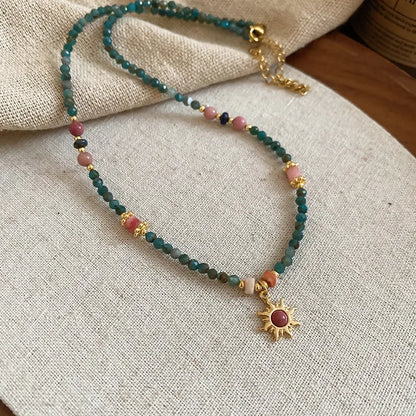 Geometric sun stone pendant on a freshwater pearl necklace with gold and blue electroplated finish.