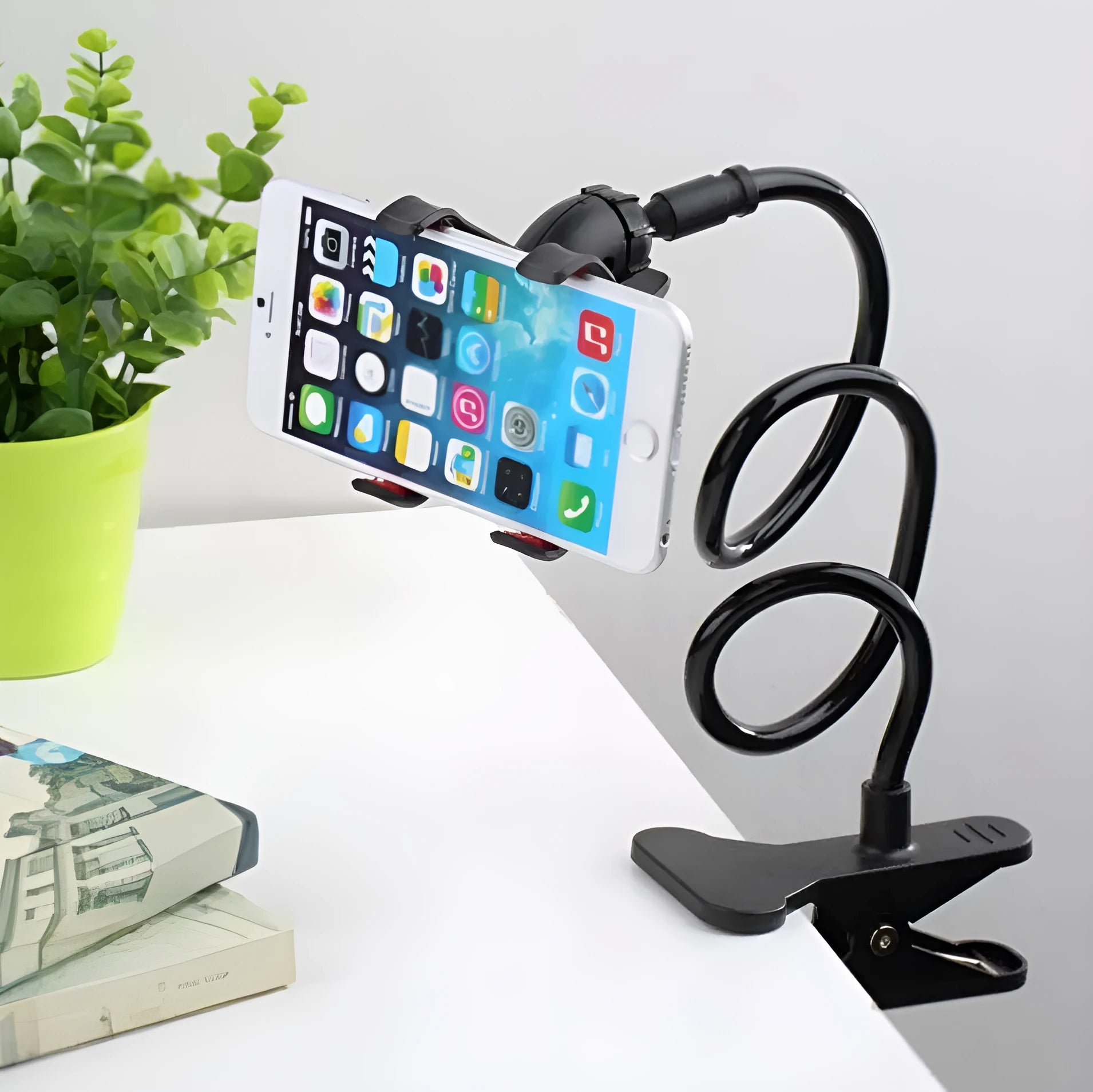 Black flexible long arm phone holder with V-clip holding a smartphone, bent over a bedside table