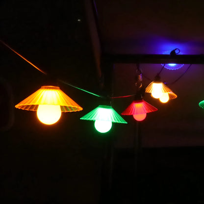 Outdoor LED string lights with white flower-shaped globes, shown illuminating a garden patio at dusk.