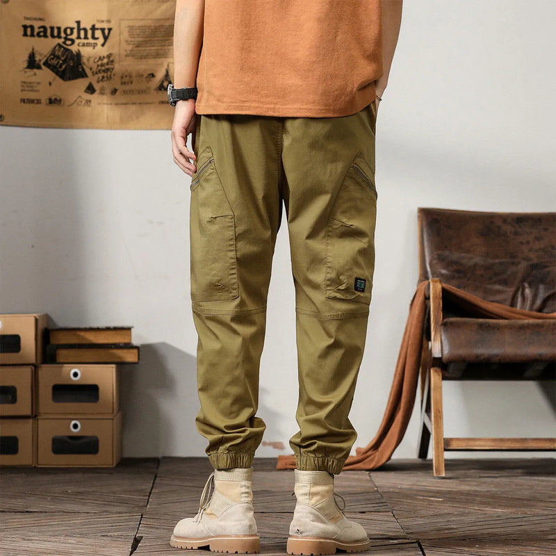 Men's loose tapered harem pants with ankle band in cotton fabric, mid waist design with zip placket opening, four seasons trousers in black coffee khaki peacock green colours, casual Korean style trousers with small leg opening