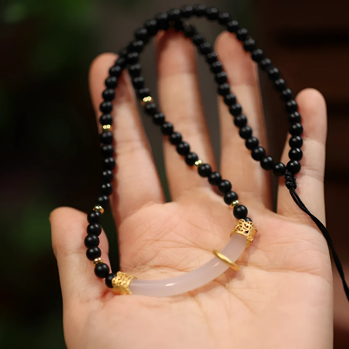 Close-up of a U-shaped necklace with frosted black agate, white chalcedony, and a 925 silver pendant on a beaded chain.