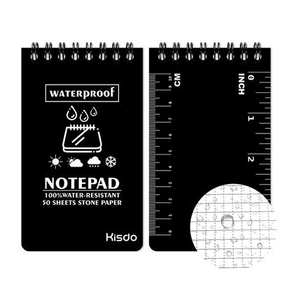 Spiral-bound waterproof notepad in camouflage colour, open on a wooden surface with a pen.