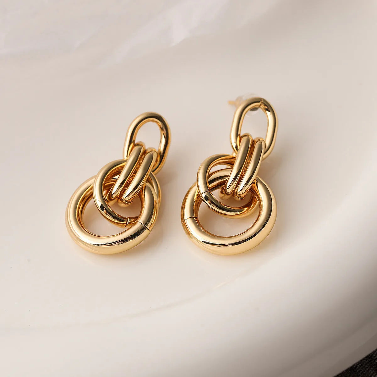 A pair of gold-coloured geometric drop earrings with irregular shapes, made from copper.