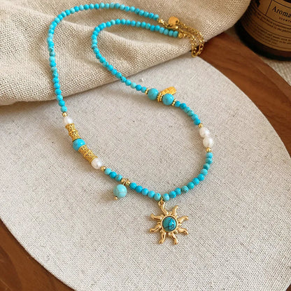 Geometric sun stone pendant on a freshwater pearl necklace with gold and blue electroplated finish.