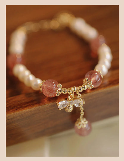 Women's strawberry quartz crystal bracelet with a decorative bow charm on a wrist.