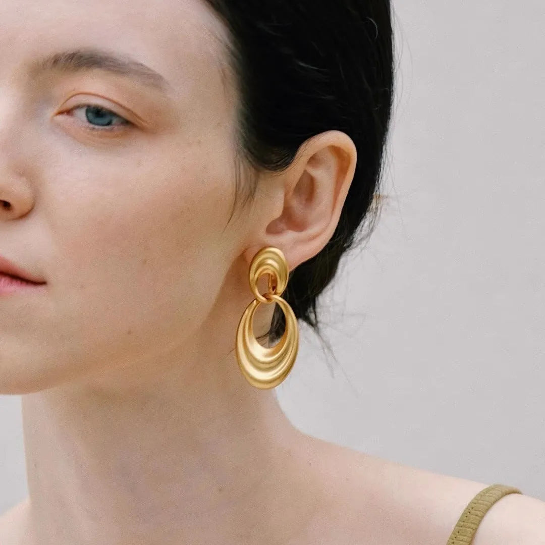 A pair of gold-coloured U-shaped women's earrings with a double circle design on a plain background.