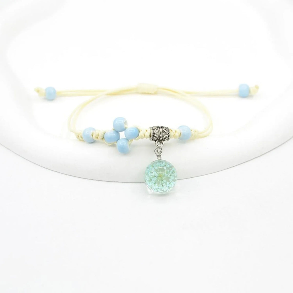 Close-up of a hand-woven bracelet with a large 1.4cm glass bead containing colourful dried flowers.