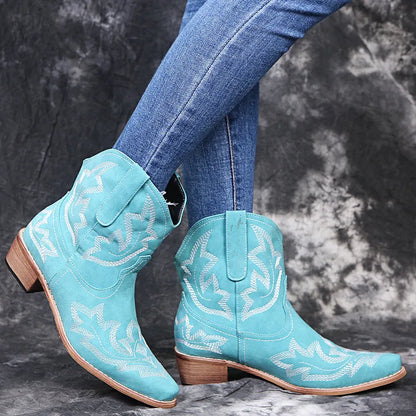 Blue women's cowboy ankle boots with embroidery and a low wedge heel on a wooden floor.