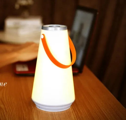 White rechargeable LED lantern with USB cable on a bedside table.