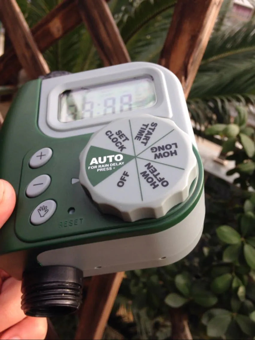Green digital garden hose timer with large display shown connected to an outdoor tap.