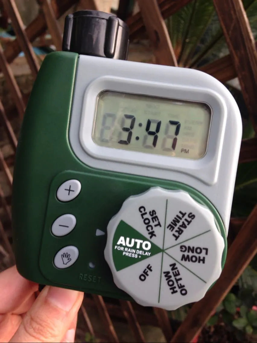 Green digital garden hose timer with large display shown connected to an outdoor tap.