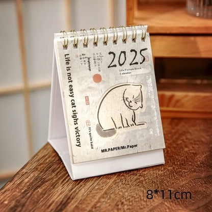 Set of four different themed 2025 mini paper desk calendars on a desk.