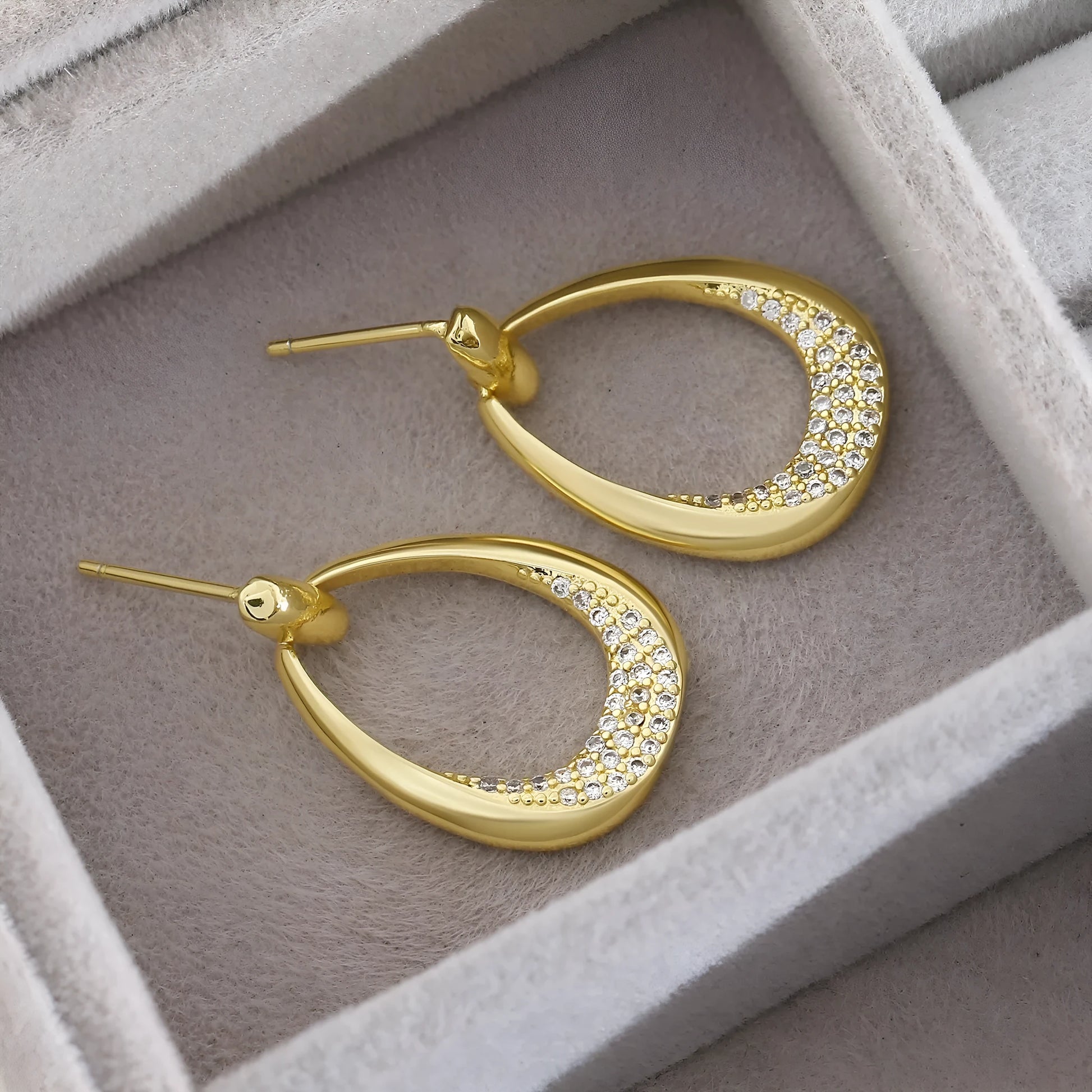 Women's yellow gold geometric drop earrings with oval and round elements on a white background.