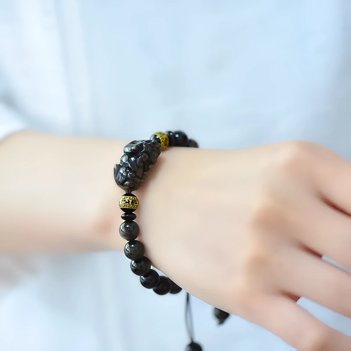 Handmade golden obsidian Pi Xiu bracelet with Chinese zodiac design on wrist.
