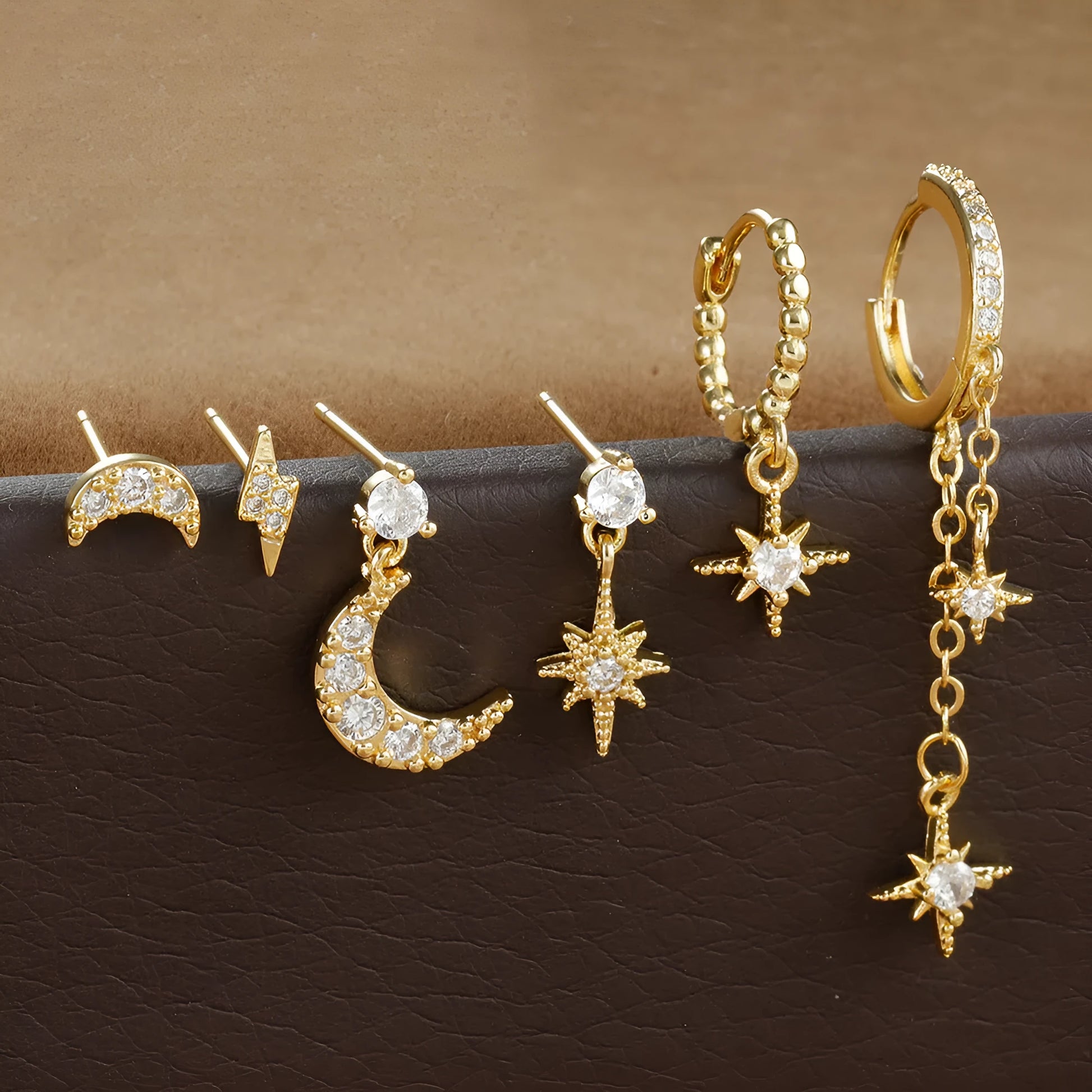 Set of six gold-coloured XINGX chain tassel stud earrings with zircon details on a flat surface.