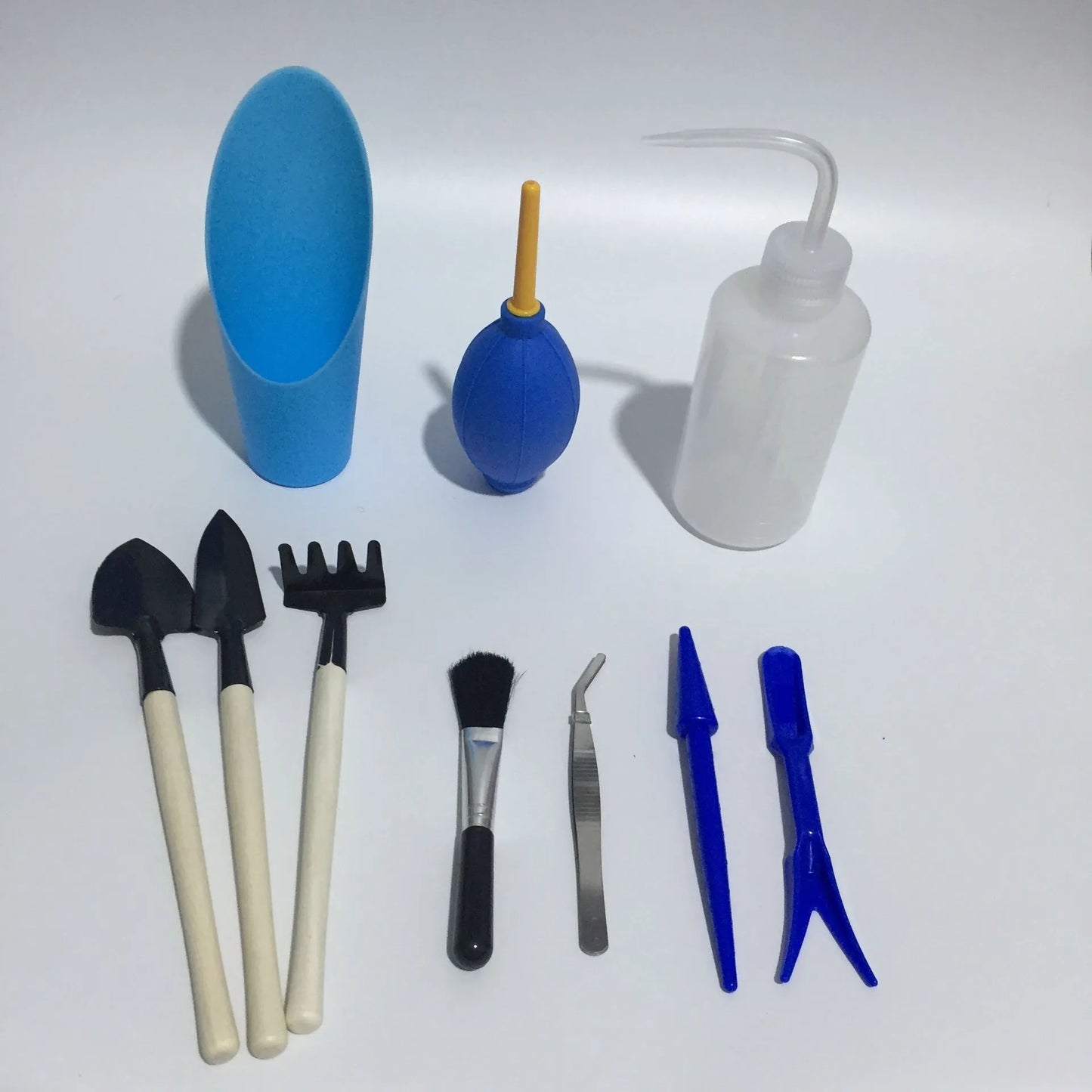 Succulent gardening tool set showing mini shovel, watering can, tweezers, and rake on a table.