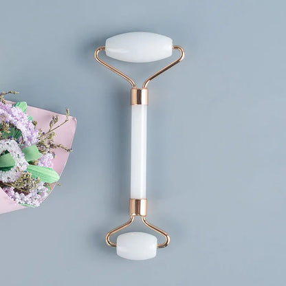 White jade facial roller with double-headed claw design and matching scraping board on dark surface