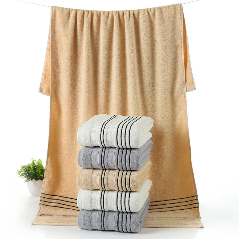 Household pure cotton towel set showing one large bath towel and two smaller hand towels in a neutral colour like grey or khaki.