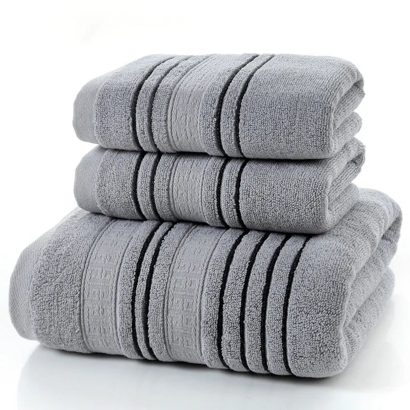 Household pure cotton towel set showing one large bath towel and two smaller hand towels in a neutral colour like grey or khaki.