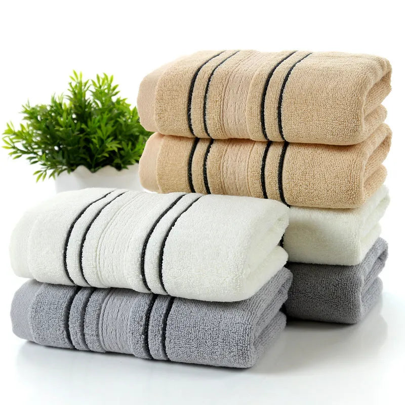Household pure cotton towel set showing one large bath towel and two smaller hand towels in a neutral colour like grey or khaki.