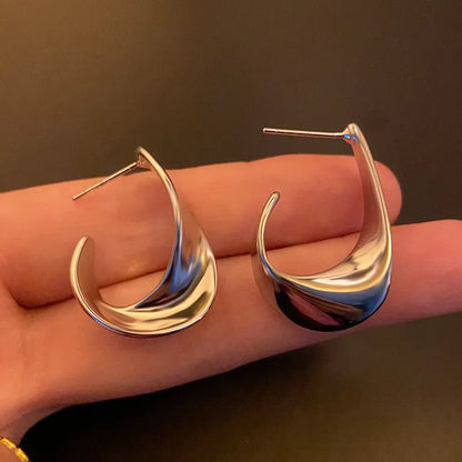 A pair of gold twisted geometric metal earrings with a round detail on a white background.