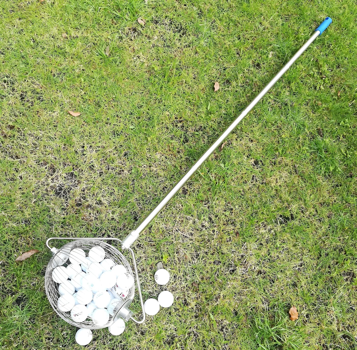 Metallic coloured stainless steel golf ball picker on a green surface.