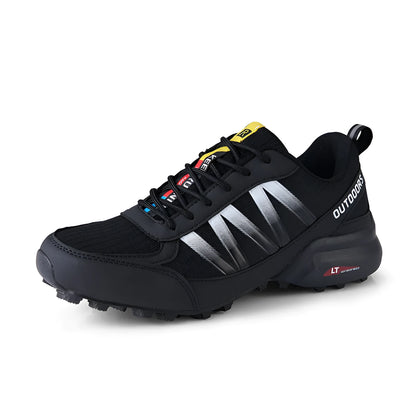 Men's black mountaineering sneakers with a rubber sole and lace-up front on a rocky surface.