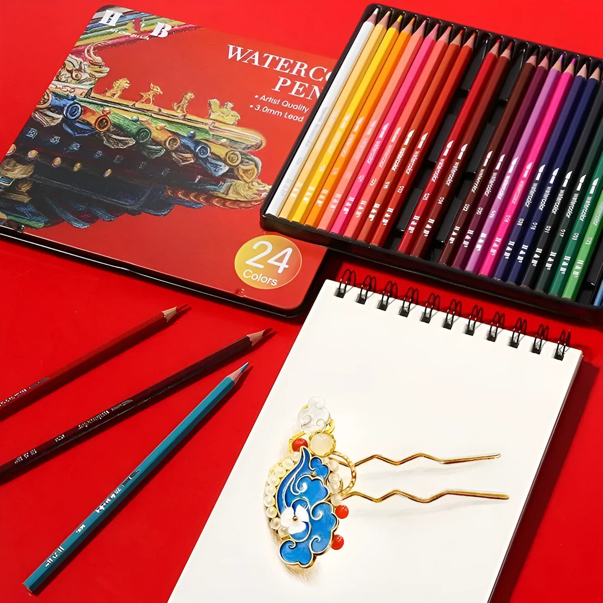 Metal tin box open to show 24 water-soluble coloured pencils with brush tips in assorted colours.