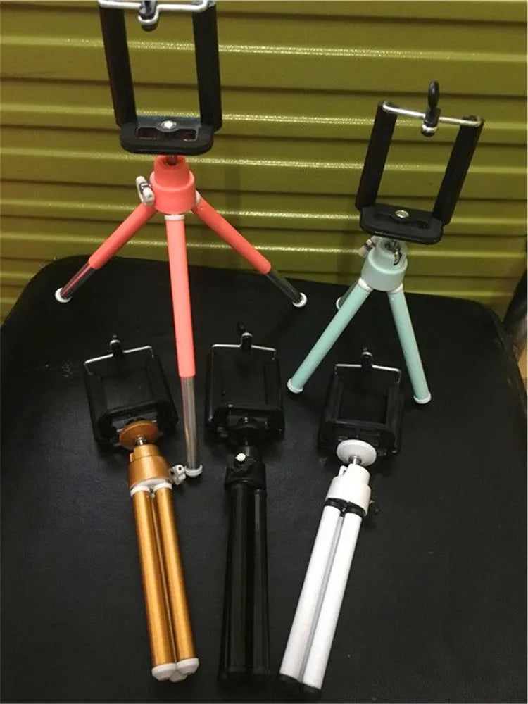 Black adjustable desktop phone holder with extended arm on a wooden desk, holding a mobile phone.