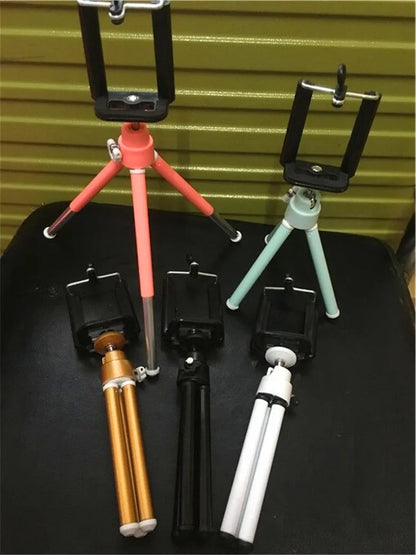 Black adjustable desktop phone holder with extended arm on a wooden desk, holding a mobile phone.