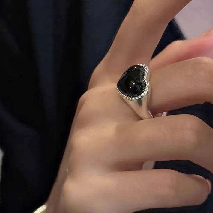Adjustable sterling silver ring with a heart-shaped black agate stone in a niche setting on a woman's finger.