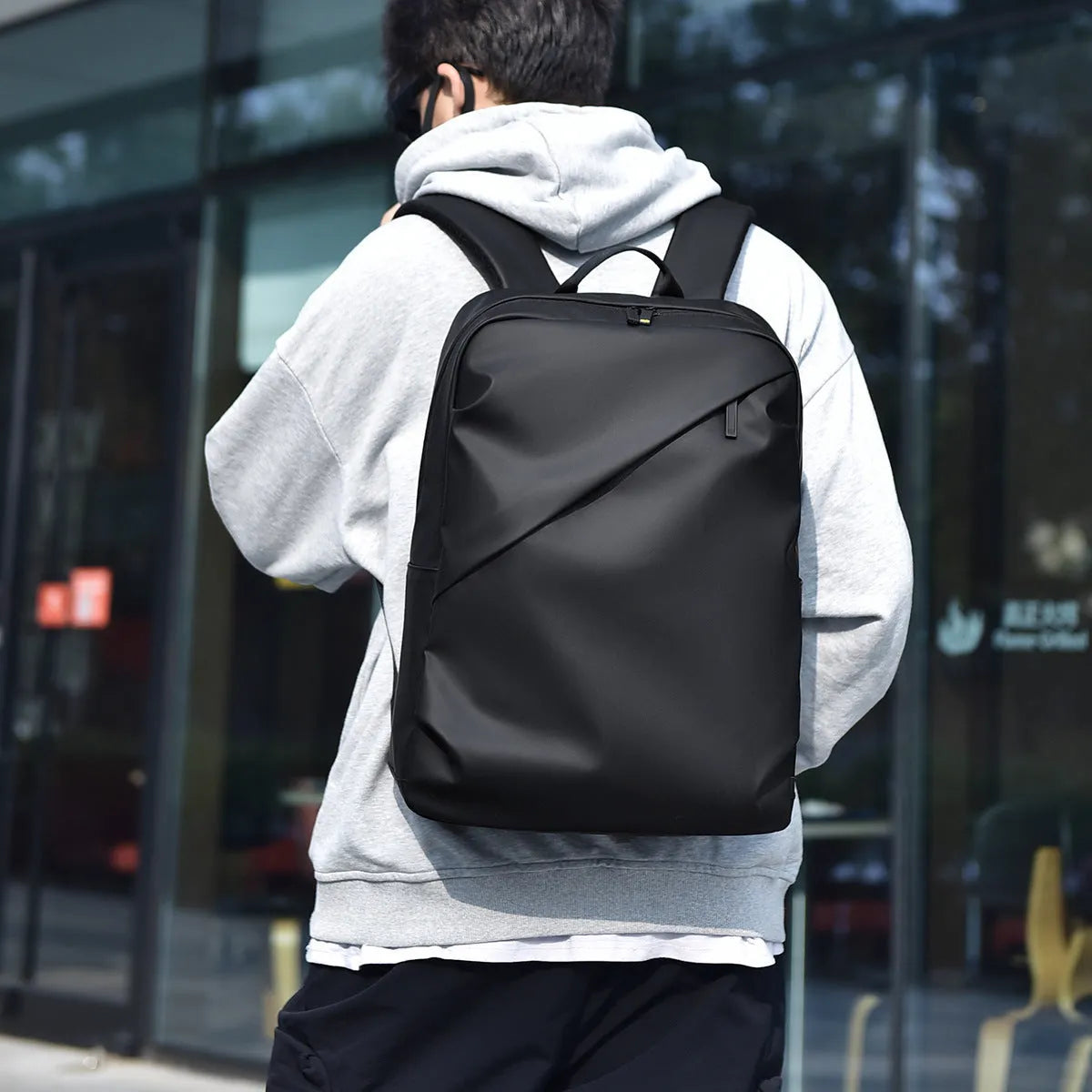 Large black waterproof PU leather laptop backpack with sewing thread details on a simple design.