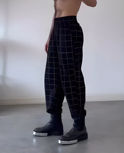Man wearing grey plaid trousers with a distinctive apron-front design detail.