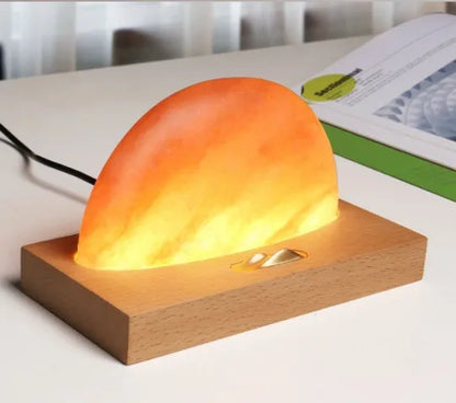 Natural crystal salt lamp with wooden base on a table, wirelessly charging a smartphone.
