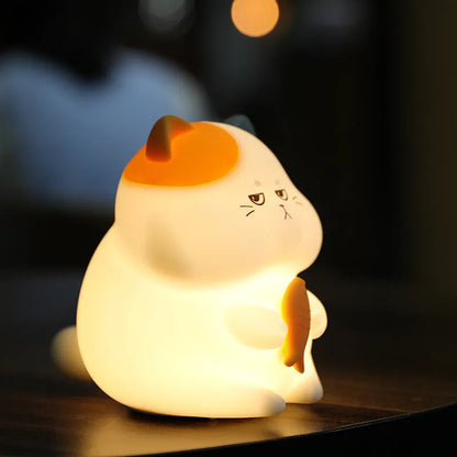 Yellow cartoon Greedy Cat desktop night light with plug, shown on a wooden desk.
