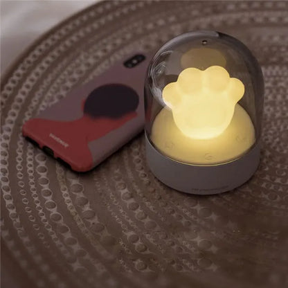 Grey cat paw shaped night light with USB port, glowing softly on a wooden surface.