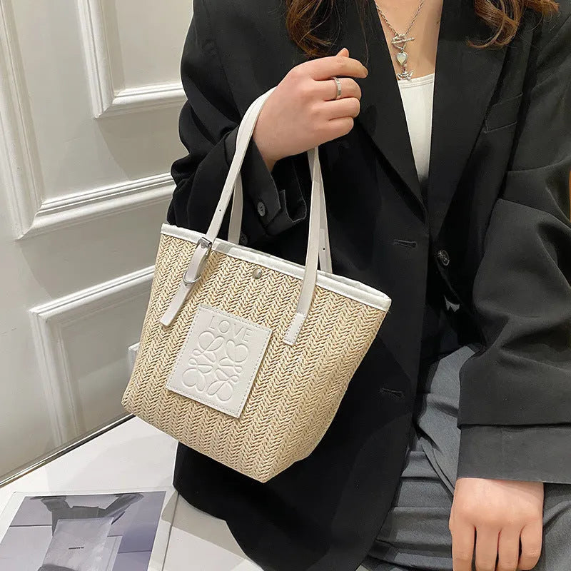 White woven straw women's shoulder bag with a three-dimensional pocket and a black handle.