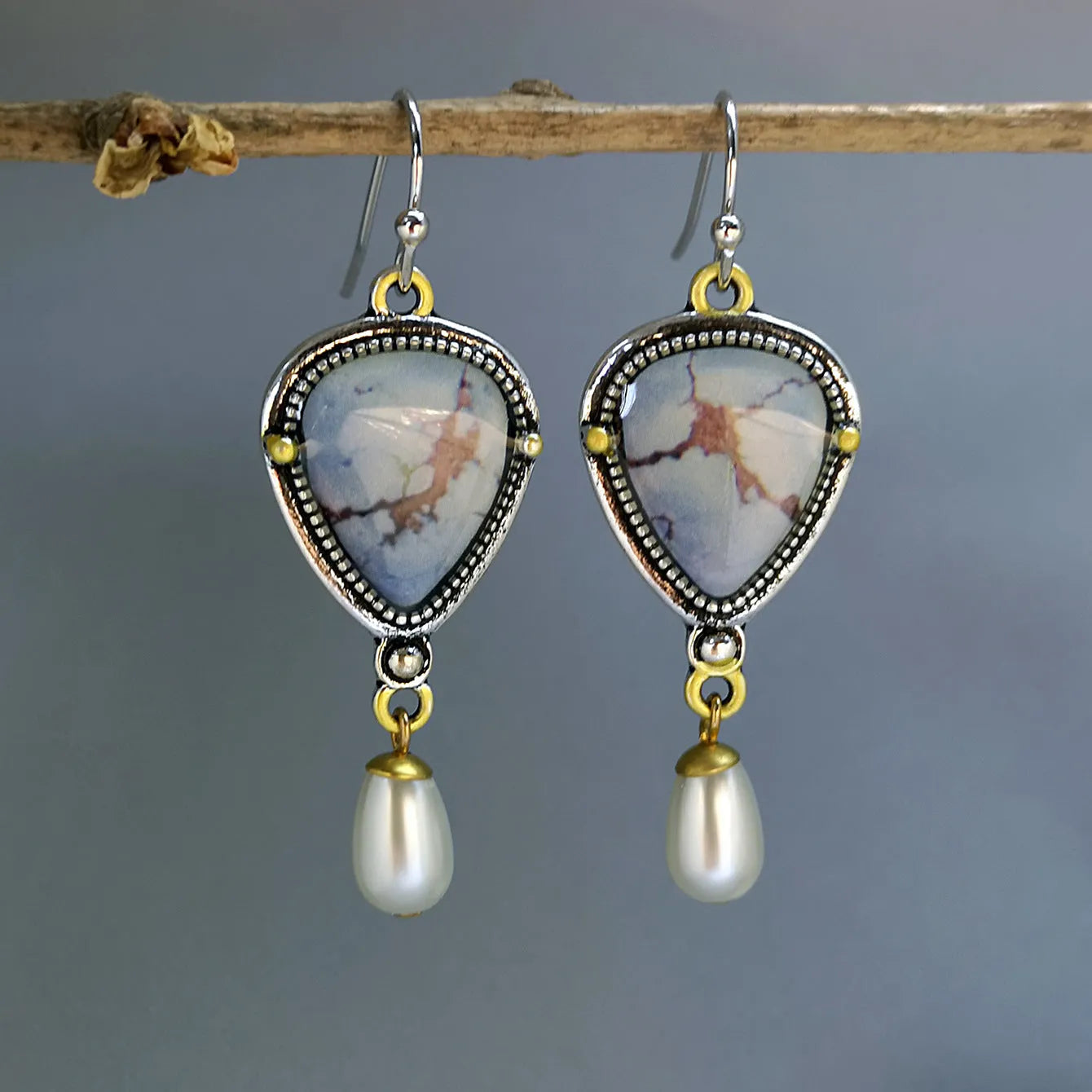 Close-up of retro blue geometric drop earrings with a synthetic blue opal stone and white pearl accent on an electroplated metal frame.