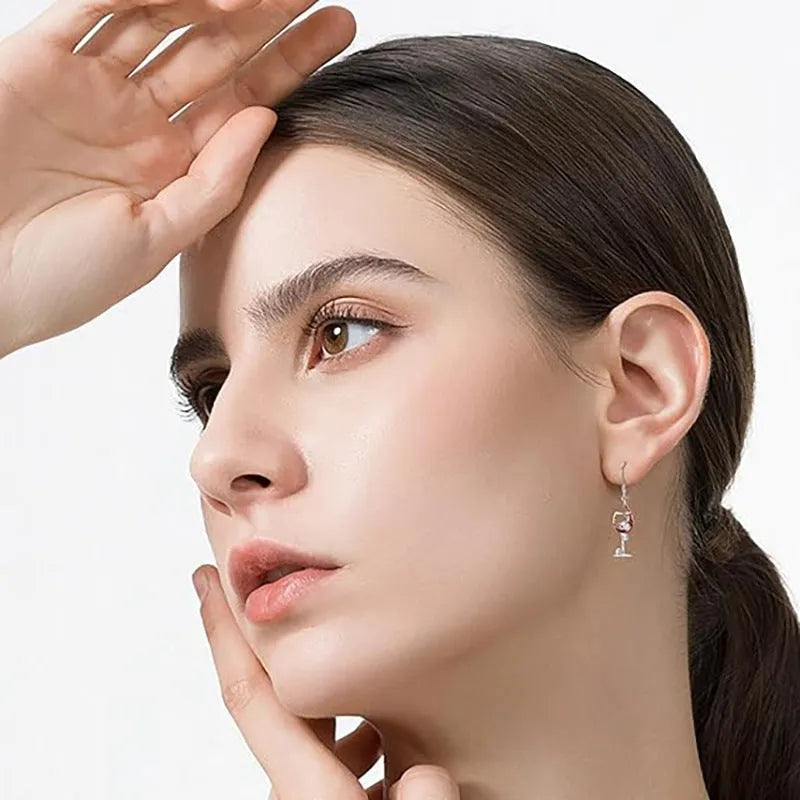 Close-up of a pair of silver-toned geometric earrings combining a skull motif with a wine glass shape.