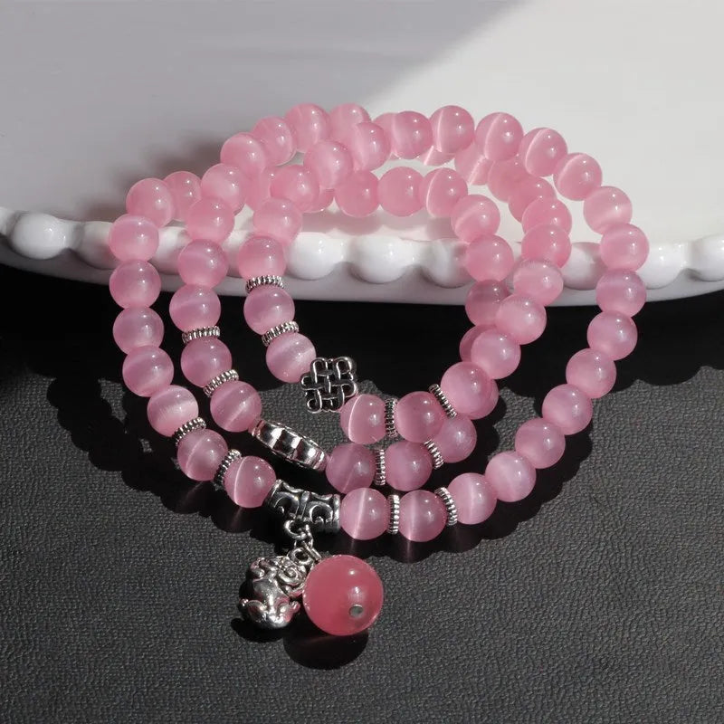 Close-up of a women's opal cat eye bracelet with three geometric rings and a lucky cat charm on a long, adjustable cord.