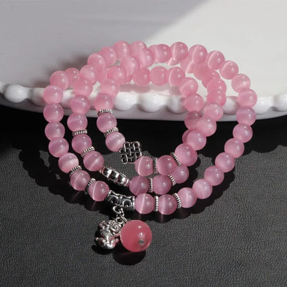Close-up of a women's opal cat eye bracelet with three geometric rings and a lucky cat charm on a long, adjustable cord.