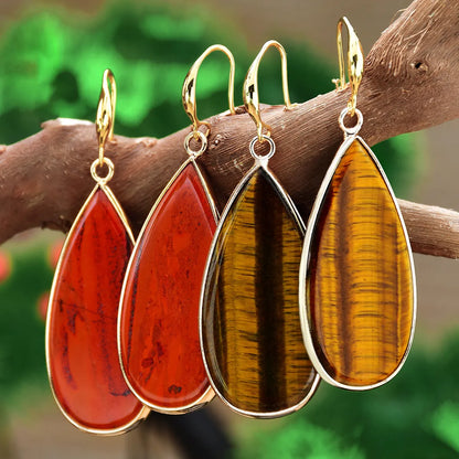 Handmade vintage long water drop earrings with tigereye stone and sterling silver hooks on a textured background.