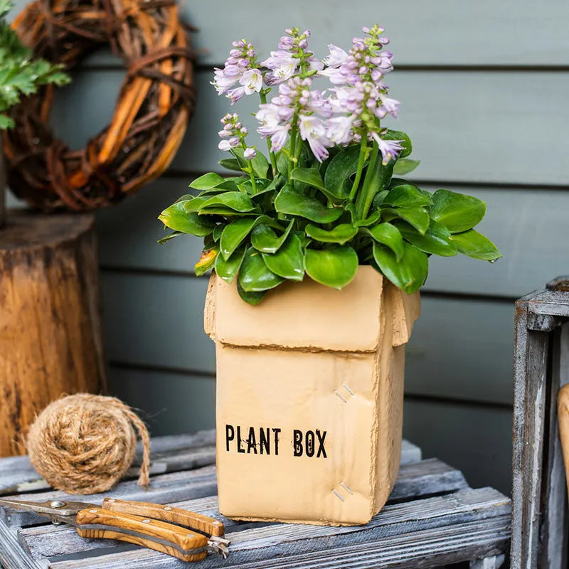 A grey cement flowerpot with a folded paper box design, shown with a drainage hole in its base.